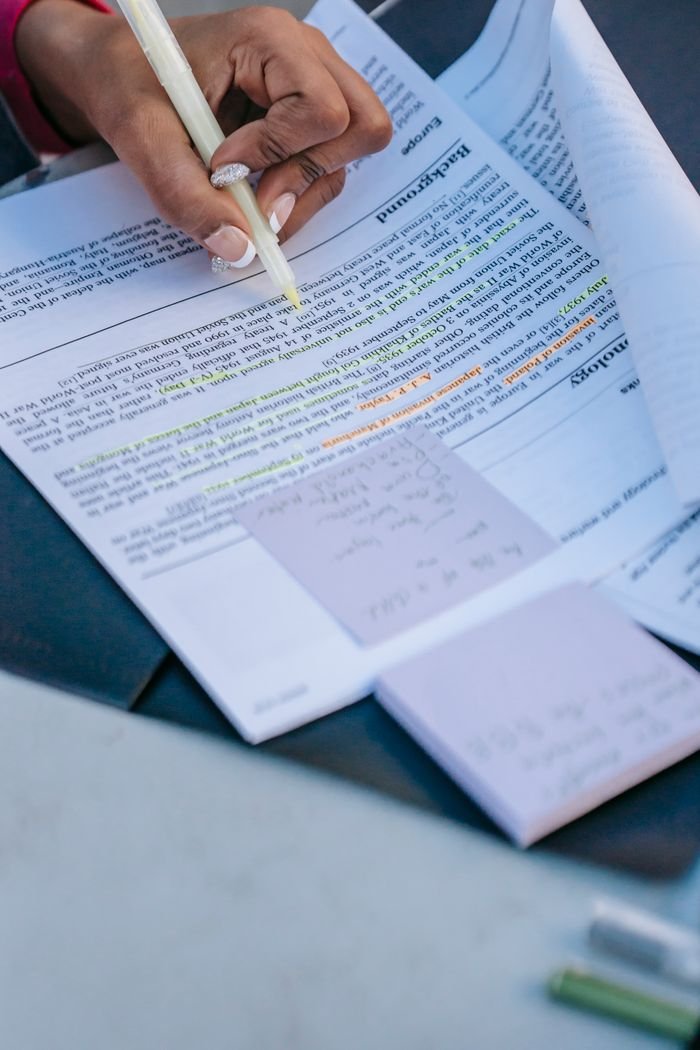 Crop anonymous ethnic female student learning project and using text marker for underlining information in document in daytime