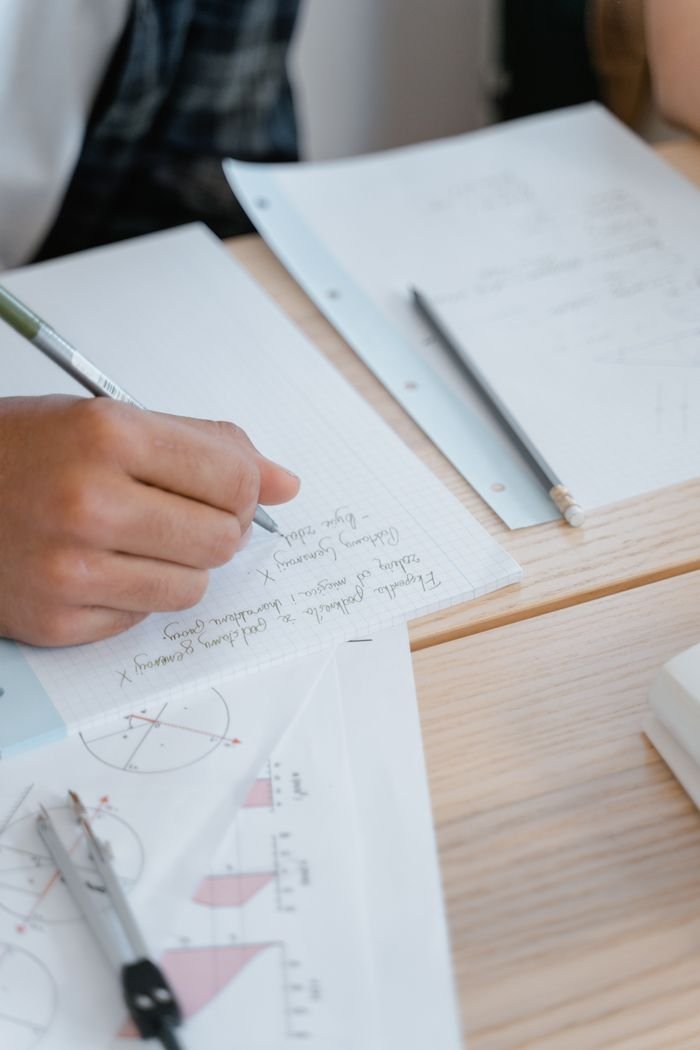 Close-up of a student's hand writing notes during a study session with geometry papers.